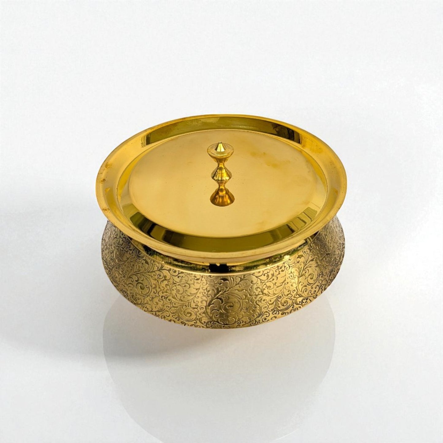 Side‑angled view of a brass handi with its lid on, highlighting the ornate exterior engraving and lid finial.
