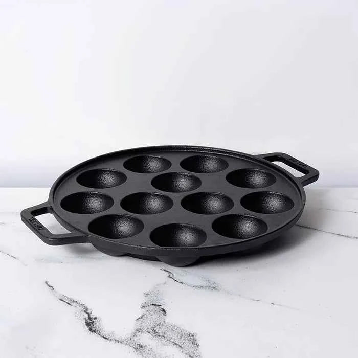 Meyer Cast Iron Appam Pan with twelve round molds and dual handles on white marble surface