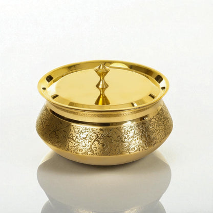 Decorative etched brass handi with lid displayed on a marble surface under warm sunlight.