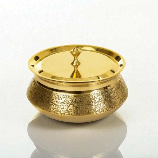 Decorative etched brass handi with lid displayed on a marble surface under warm sunlight.