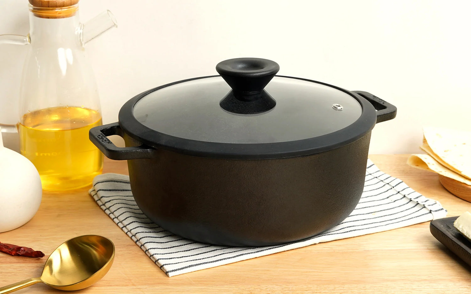 Meyer cast iron sauteuse with lid on a wooden surface with kitchen items around