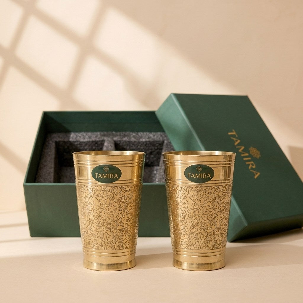 Two pure brass glasses with etched floral scrollwork in front of their green gift box