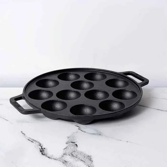 Meyer Cast Iron Appam Pan with twelve round molds and dual handles on white marble surface