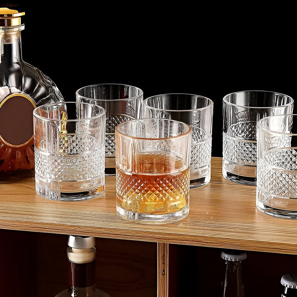 RCR Brillante whisky glass set displayed on a wooden shelf with whiskey and a bottle