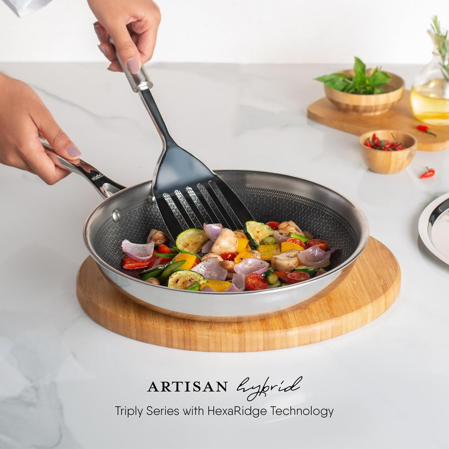 Stahl Artisan Hybrid Triply Fry Pan with Lid 24 cm showcasing sautéed vegetables and a spatula